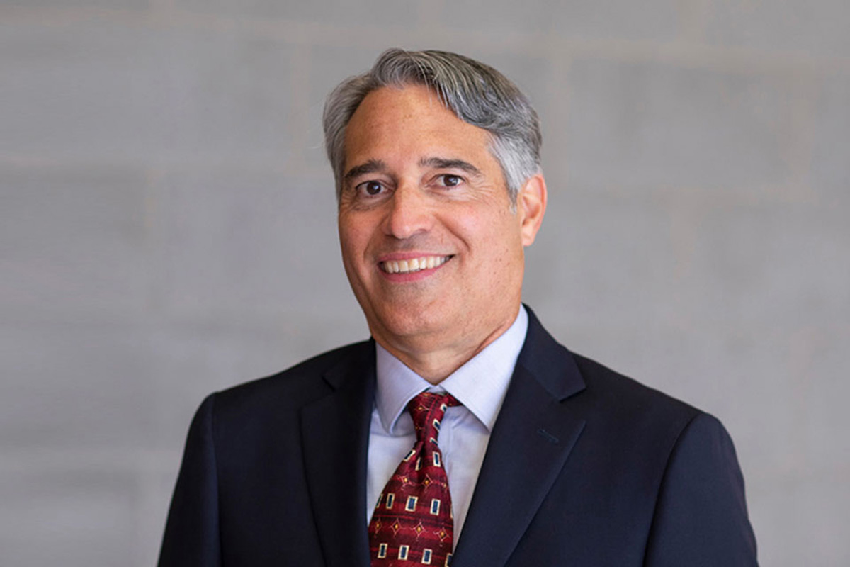 Dr. René Vellanoweth wearing a navy suit with a blue shirt and red patterned tie.